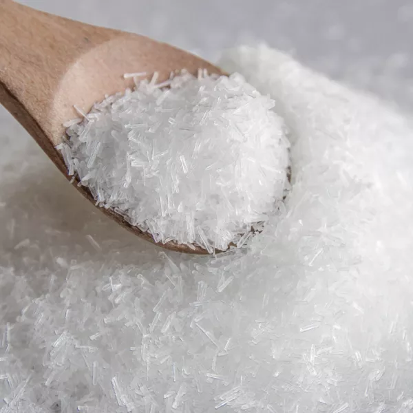 Close-up of a wooden spoon holding crystalline white granules, with more of the same granules scattered below.