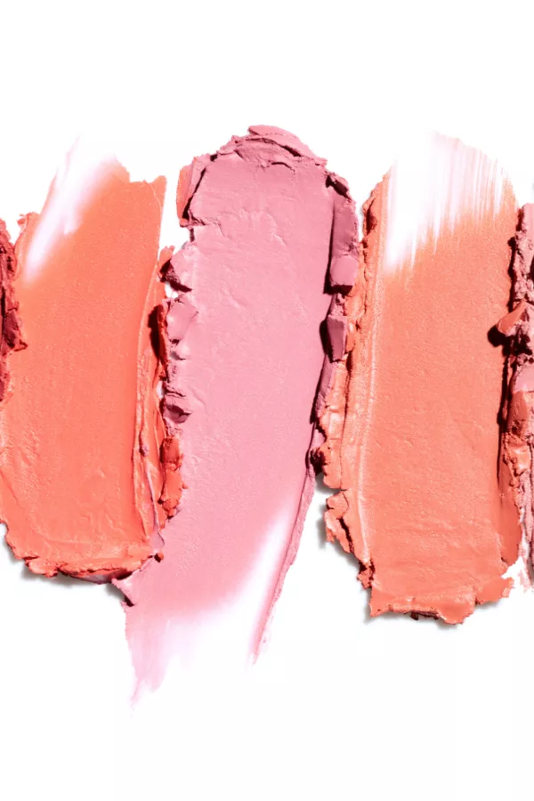 Three smears of creamy makeup in coral, pink, and peach shades on a white background.