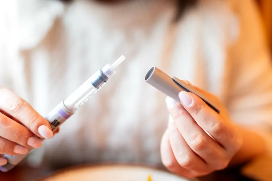Close-up of a person removing the cap from an insulin pen injector, with both hands visible.