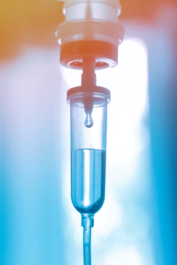Close-up of an intravenous (IV) drip chamber with liquid and a droplet, used for medical fluid administration.
