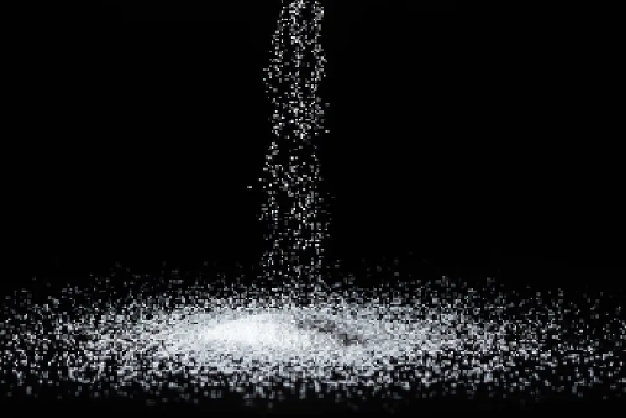 A stream of granulated white salt falls onto a growing pile against a black background.