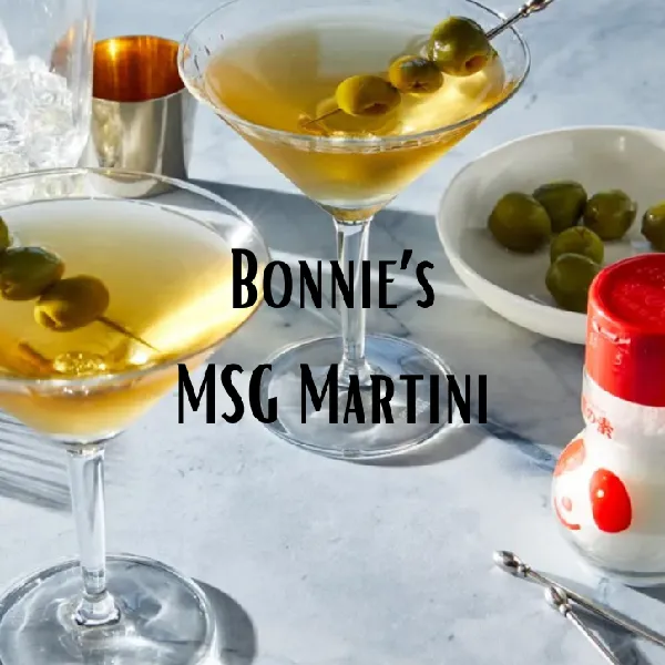 Two martini glasses with olives, a bowl of green olives, a shaker, and a container of MSG are arranged on a table. Text reads: "Bonnie's MSG Martini.