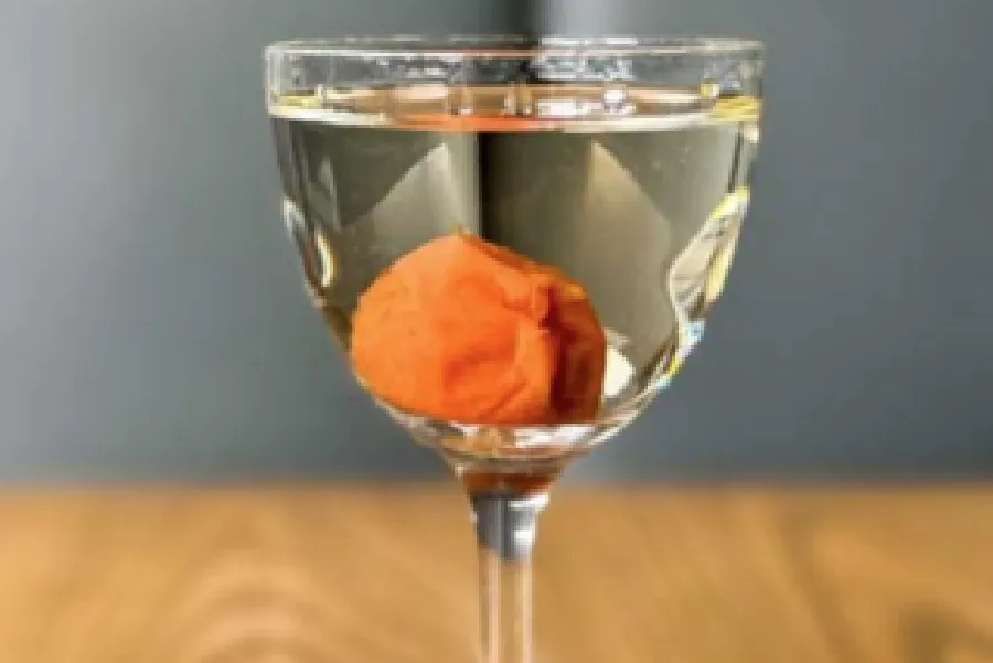 A clear glass filled with a transparent liquid and a single orange-red pickled plum at the bottom.