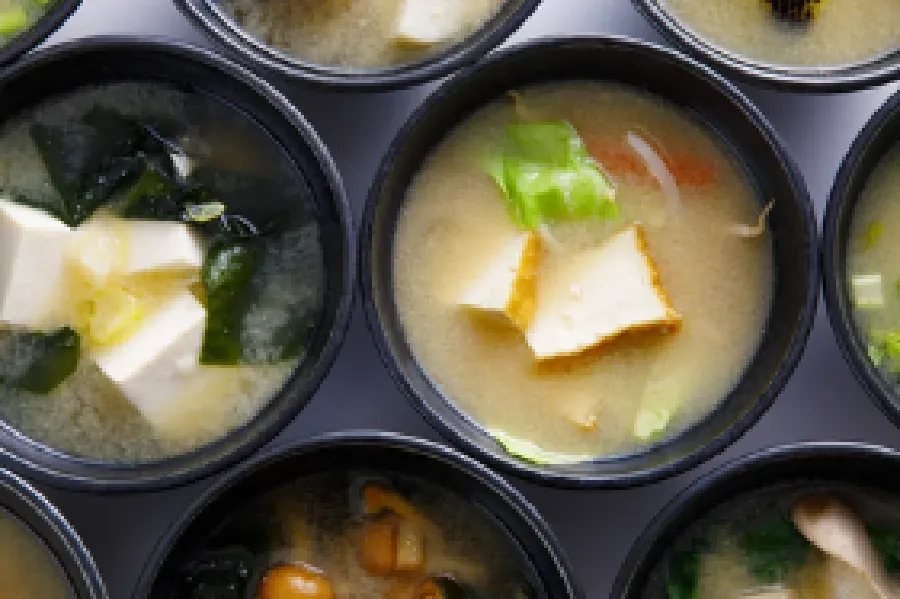 Several bowls of miso soup with various ingredients, including tofu, seaweed, mushrooms, and vegetables, arranged in a grid pattern.