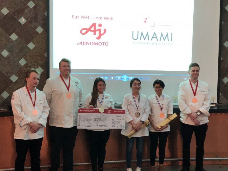 Six chefs wearing medals stand in a row, three holding prizes, in front of a screen displaying the Ajinomoto and Umami Information Center logos.