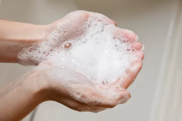 Two hands are cupped together holding a large amount of soapy foam, indicating handwashing with soap and water.