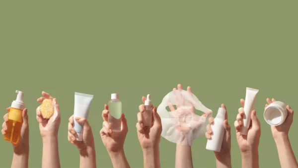 Several hands hold up various skincare products, including bottles, tubes, a sponge, a dropper, and a face mask, against a plain light green background.