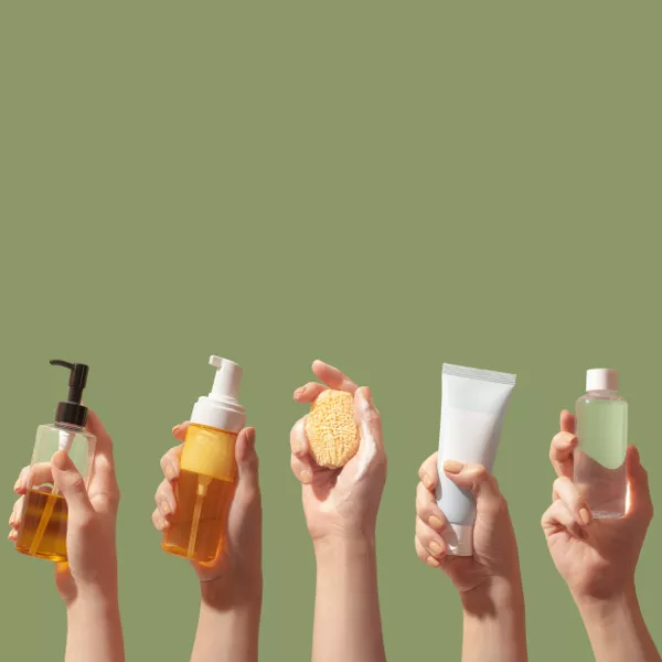 Five hands hold skincare products, including pump bottles, a sponge, a tube, and a clear bottle, against a plain olive green background.