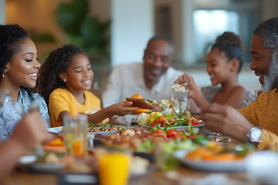 A family of four sits at a dining table, smiling and sharing a meal with various dishes and drinks.
