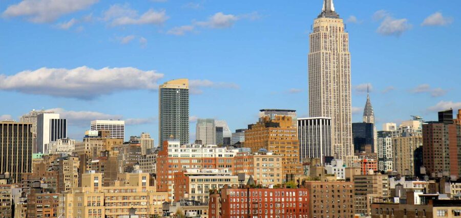 City skyline with various high-rise buildings under a blue sky with scattered clouds, including a prominent skyscraper in the center.