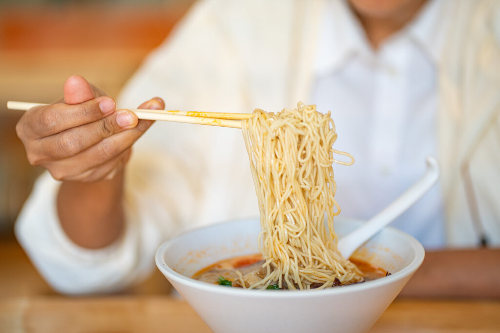 Crop anonymous female with chopsticks eating yummy ramen soup with noodles and meat in black bowl at ramen restaurant.
