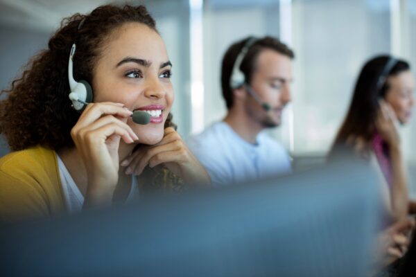 Three call center employees wearing headsets sit in a row, focusing on their conversations while working at their desks.