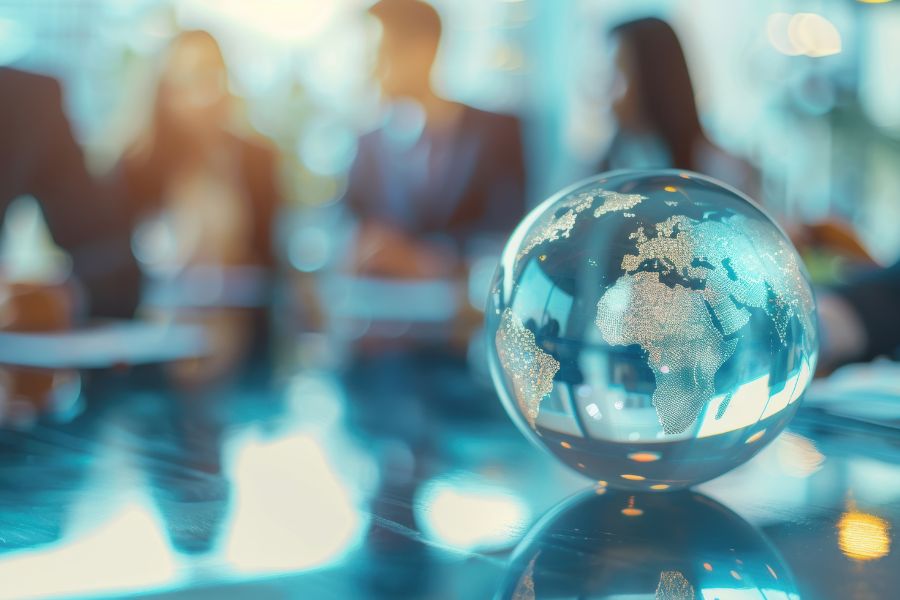 A glass globe showing Africa and Europe sits on a table with blurred people in business attire meeting in the background.