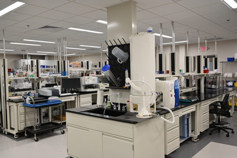 A modern laboratory with workstations, lab equipment, storage cabinets, a sink, and various scientific instruments arranged neatly around the room.
