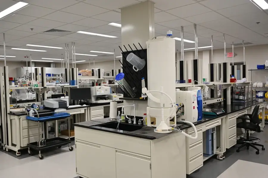 A modern laboratory with workstations, lab equipment, storage cabinets, a sink, and various scientific instruments arranged neatly around the room.